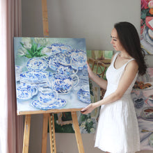 Load image into Gallery viewer, Elizabeth Alice Studio original painting art, blue and white dishes set stacked up, traditional decor, set of dishes, art for dining room, blue and white painting, art for traditional home, art for blue and white decor, art for southern traditional home, art for coastal style home, loose brush strokes acrylic painting, impressionist modern art, the artist standing next to painting on easel in studio